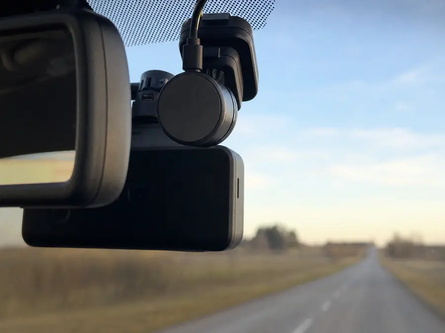 Dikiz aynası arkasındaki kamera pedine takılı yuvarlak GPS modülü; camın ardında açık kırsal yol