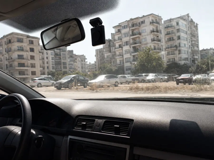 Yaz güneşi altında park etmiş araçta gösterge paneli ve ön camdaki kamera; sert gölgeler, toz